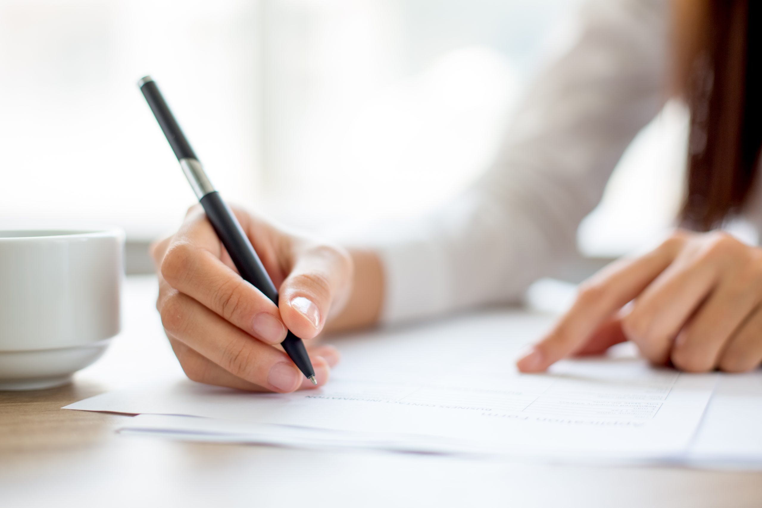 Hand of young businesswoman writing on paper or signing contract at table in office